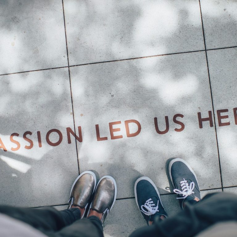 Vier Füße in Schuhen auf Asphalt mit dem Schriftzug "Passion lead us here".
