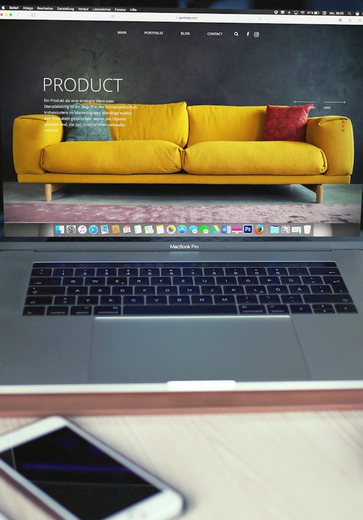 Laptop mit Anzeige eines gelben Sofas, davor ein Smartphone.